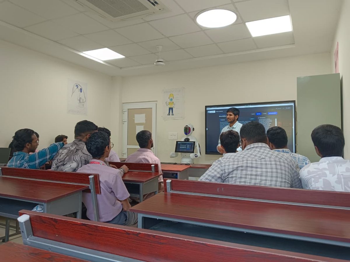 Trainees seated at benches in an industrial training institute, watching a session run from the robot and the wall screen beside it