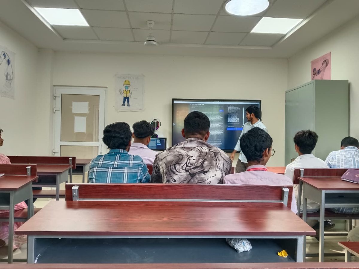 An instructor leading a session in a training institute classroom, with the robot beside the wall display