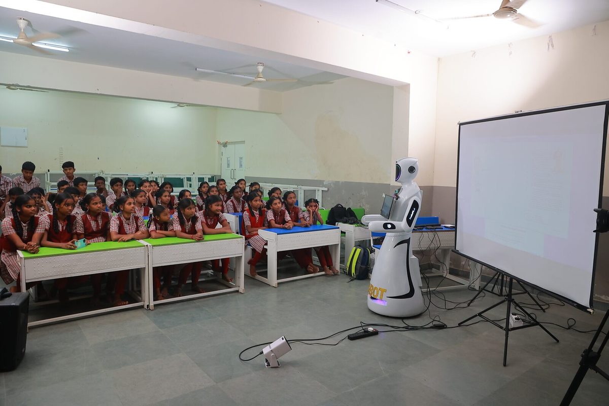 A full classroom of seated students facing EDU-BOT and a projector screen at the front of the room
