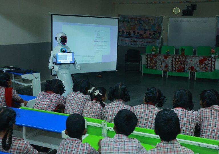 EDU-BOT running a lesson from the front of the class, the projector screen beside it showing the same material